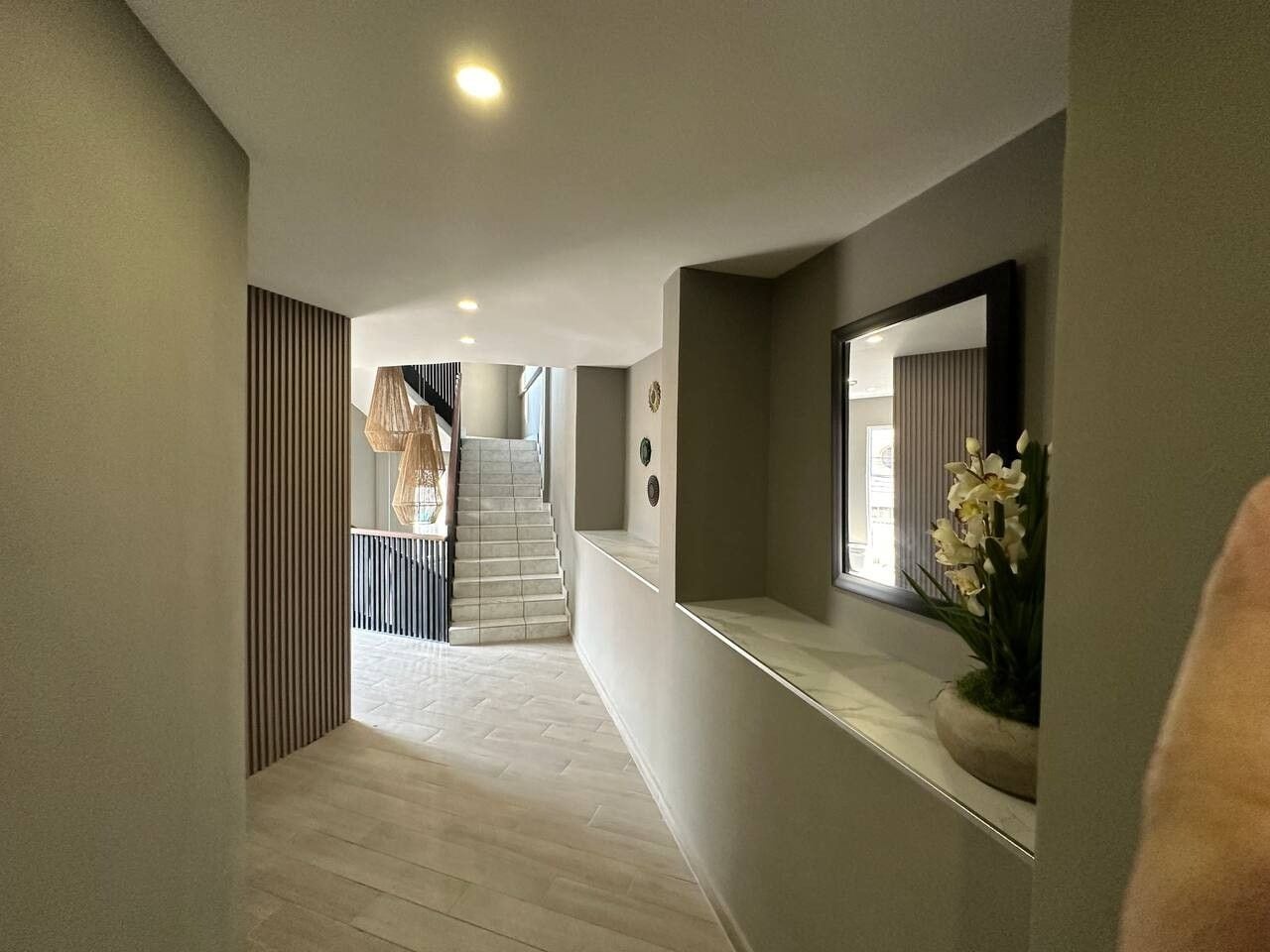 A hallway with a staircase leading to an upper floor, a wall-mounted mirror, and a potted plant.