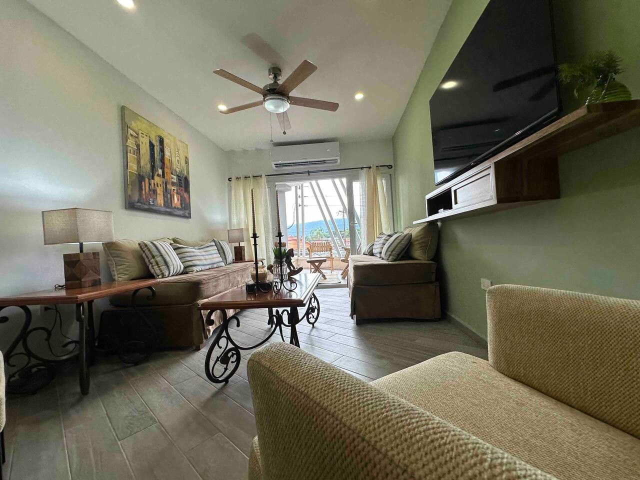 Un salon comprenant un canapé, une table basse, un téléviseur fixé au mur et un ventilateur de plafond.