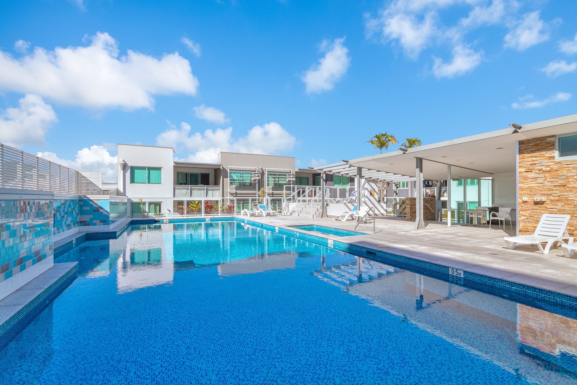 A modern hotel with a swimming pool, outdoor seating, and a clear blue sky.