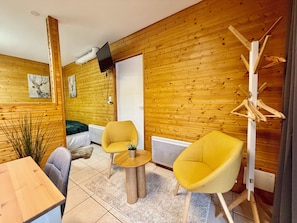 A room with wooden walls, a bed, two yellow chairs, a small table, and a mounted TV. - "The Mountain Retreat," between the lake and downtown (Xonrupt-Longemer)
