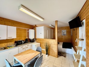 A compact kitchen with a dining area, a bed, and a mounted TV. - "The Mountain Retreat," between the lake and downtown (Xonrupt-Longemer)