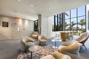 Ein moderner Coworking-Space mit bequemen Sitzgelegenheiten, einer Bar und großen Fenstern mit Blick auf Palmen.