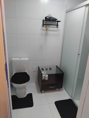 Ein kleines Badezimmer mit Toilette, einer Duschkabine aus Glas und einem Ablagebereich für Pflegeprodukte.