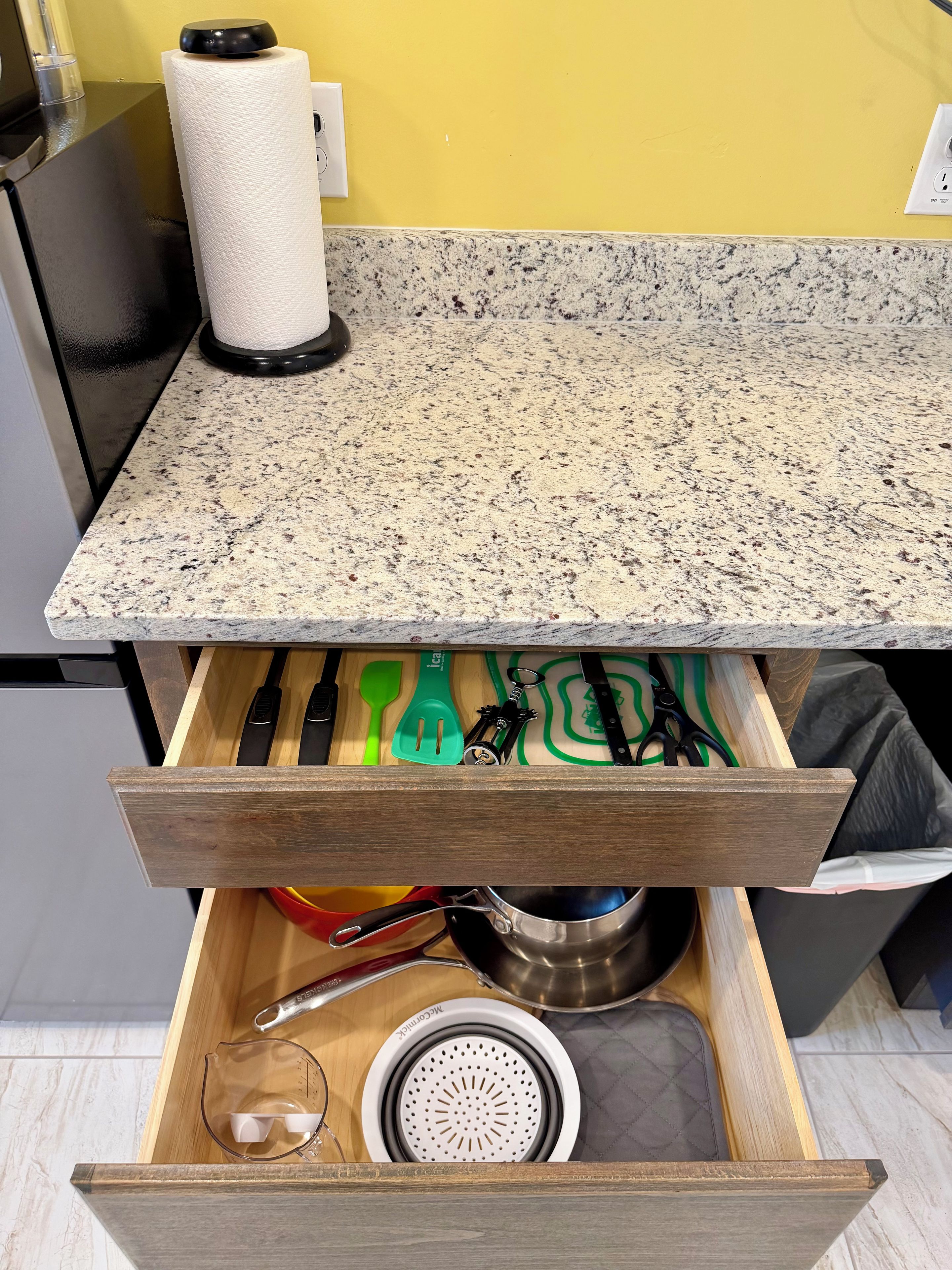 A kitchen drawer with utensils, a colander, and a pot.