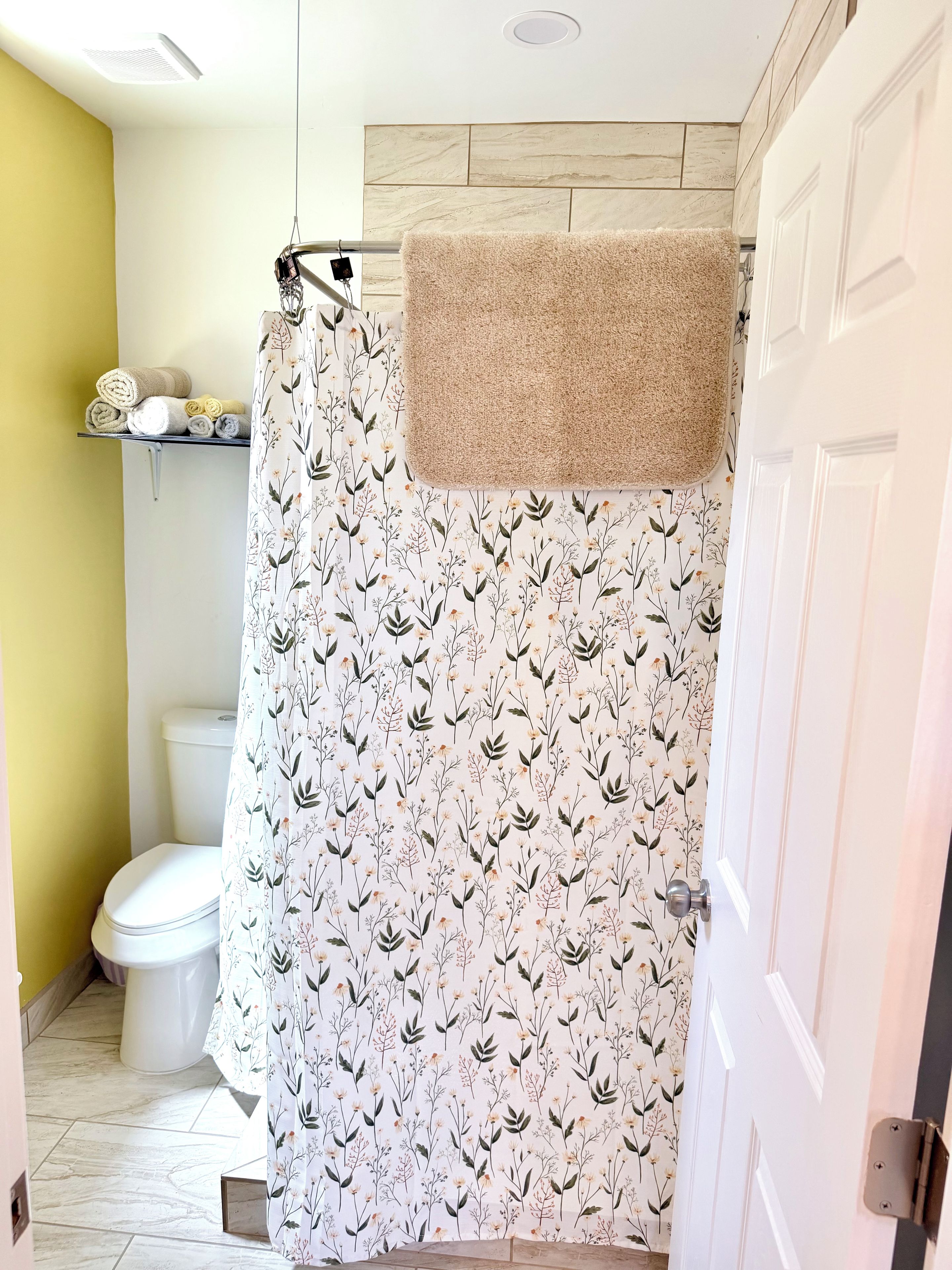 Un baño con cortina de ducha estampada con motivos florales, un inodoro y un estante con toallas enrolladas.