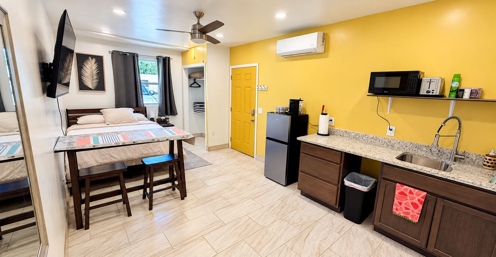 Une chambre d’hôtel compacte comprenant un lit, une petite table à manger, une kitchenette équipée d’un four à micro-ondes et un ventilateur de plafond.