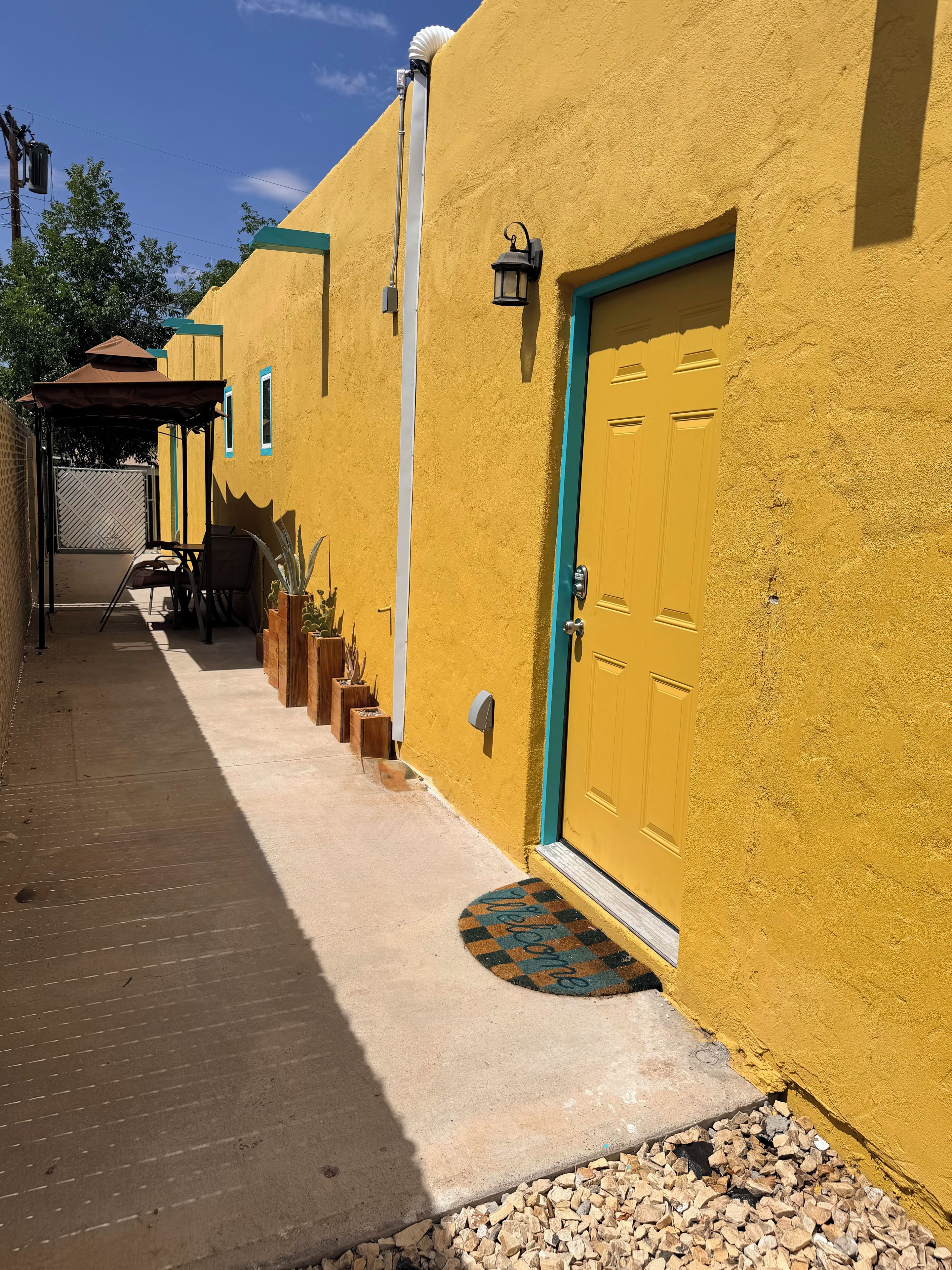 A yellow building with a door, a mailbox, and a small porch area with chairs and a table.