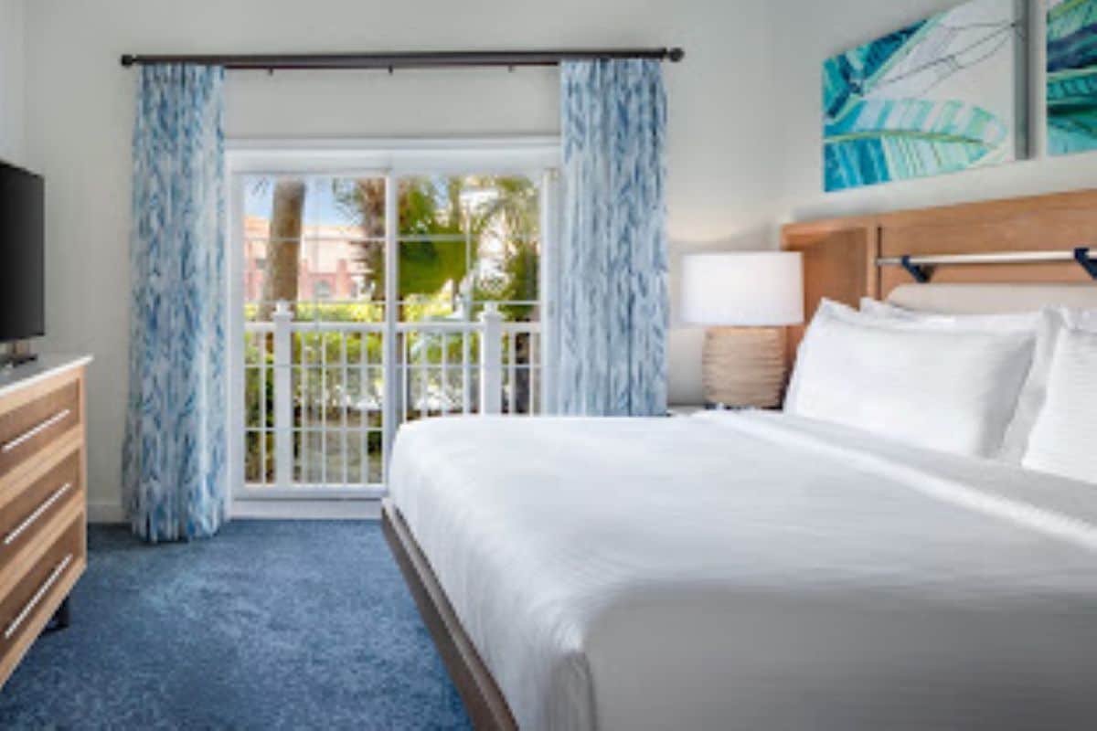 Una habitación de hotel con cama, televisión, cómoda y ventana con cortinas.