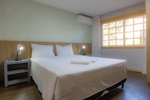 Habitación de hotel con una cama, dos mesitas de noche con lámparas, una ventana con cortinas y un equipo de aire acondicionado en la pared.