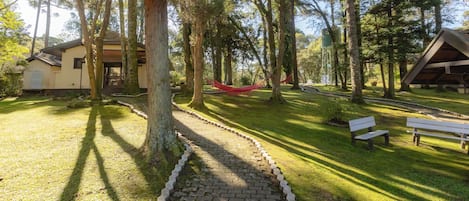 A paved pathway leading through a wooded area with benches and a hammock.