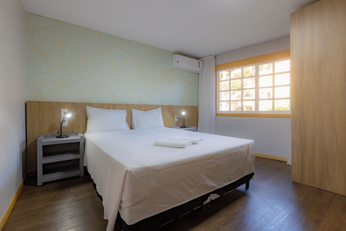Een hotelkamer met een bed, nachtkastjes, een airconditioning en een raam met uitzicht.