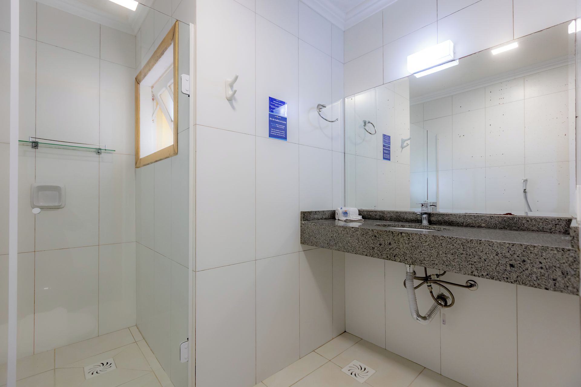 Un baño con ducha, un lavabo con encimera de granito y un espejo grande.
