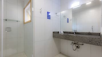 Un baño con ducha, un lavabo con encimera de granito y un espejo grande.
