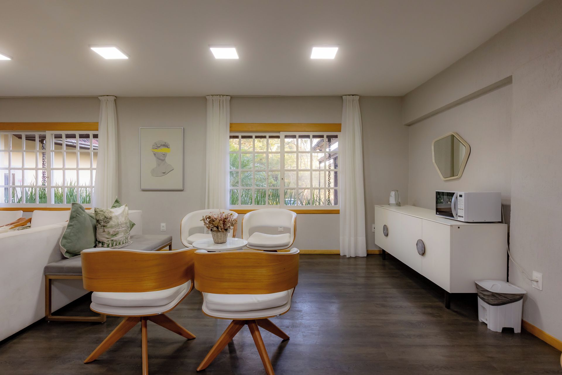 A modern living room with a sofa, two chairs, a coffee table, a cabinet with a microwave, and a window with curtains.