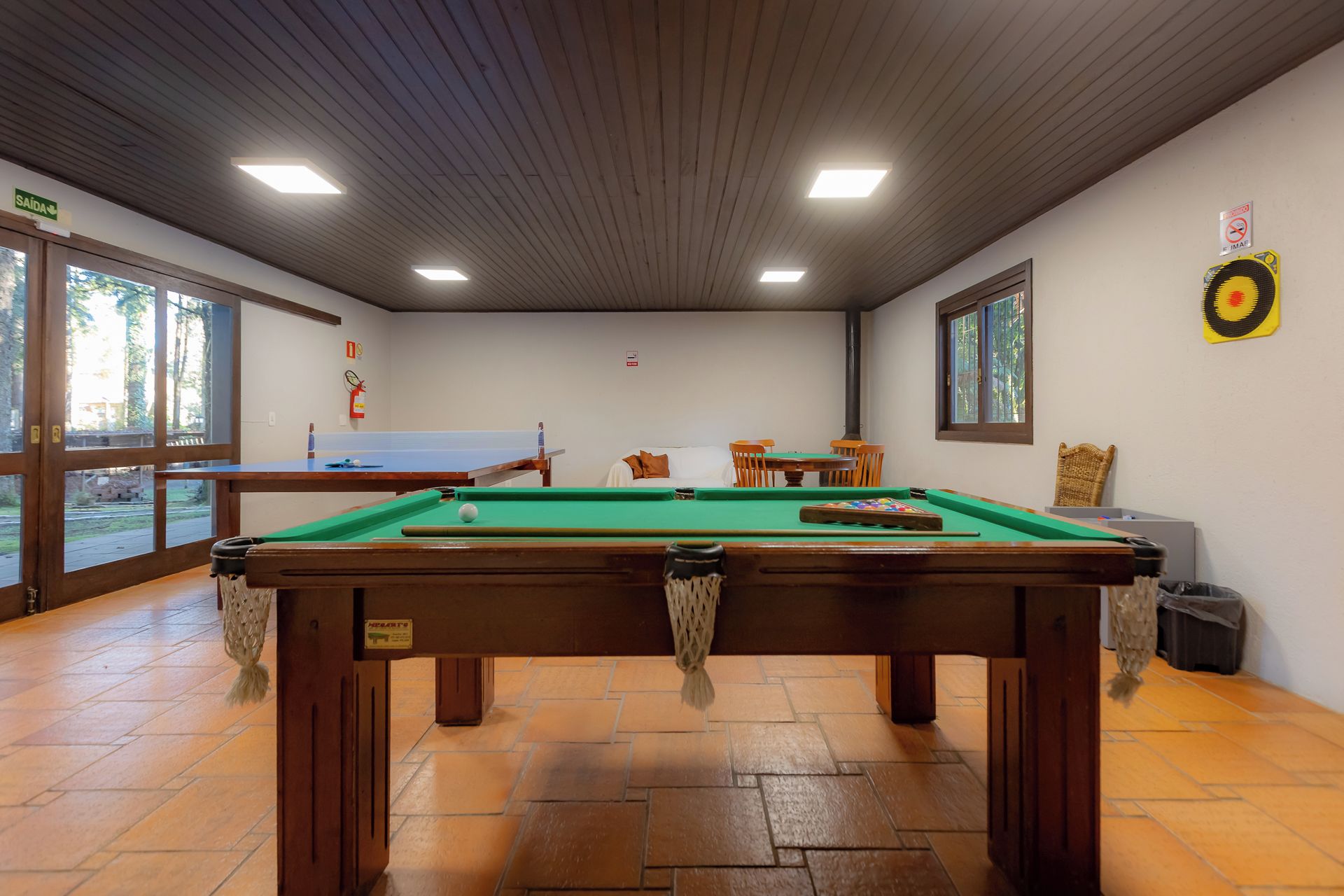 Una mesa de billar en una habitación con techo de madera y ventanas amplias.
