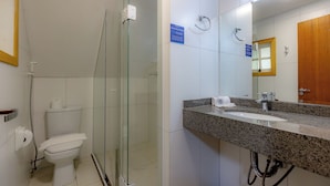 Een moderne badkamer met een douchecabine van glas, een toilet en een wastafel met een granieten blad en een spiegel.