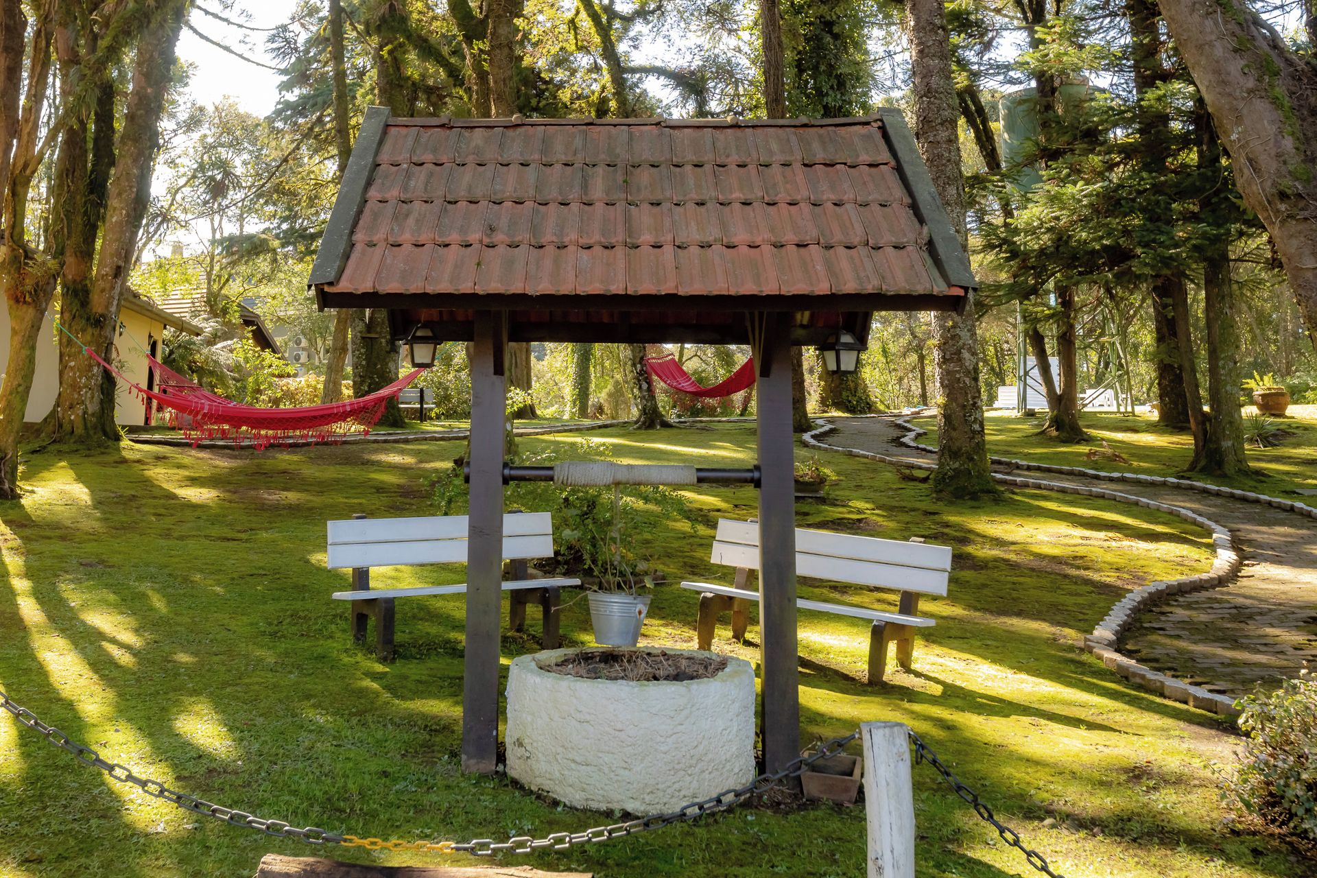 Un pabellón con techo de tejas, dos bancos y una planta en maceta en un parque.