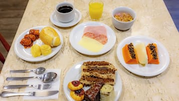Una mesa preparada para el desayuno, con tortitas, jamón y fruta.