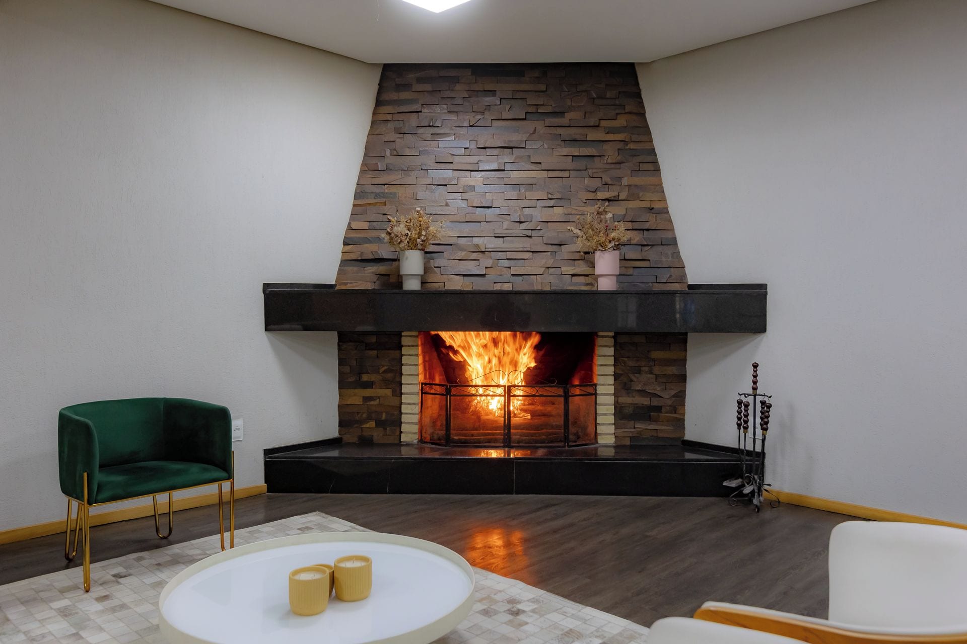A modern living room with a stone fireplace, a green armchair, a white round table with candles, and a white sofa.