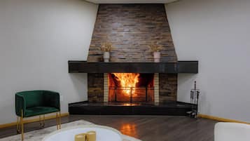 A modern living room with a stone fireplace, a green armchair, a white round table with candles, and a white sofa.