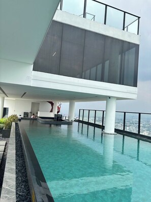 Un edificio moderno con piscina infinita en la azotea, un refrigerador con la marca Coca-Cola y vistas a la ciudad.