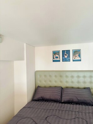 Una cama con cabecera capitonada, dos almohadas y tres cuadros en la pared.