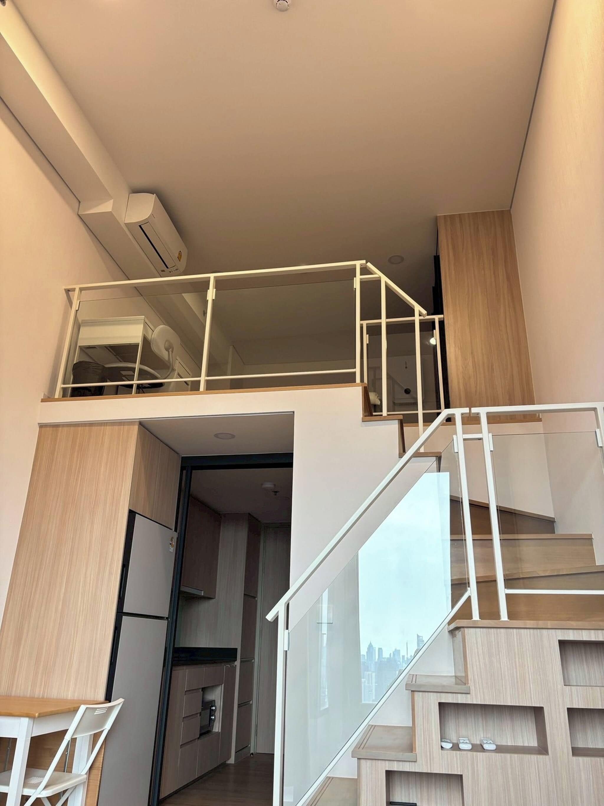 A modern apartment with a kitchen, dining area, and a staircase leading to a loft bedroom.