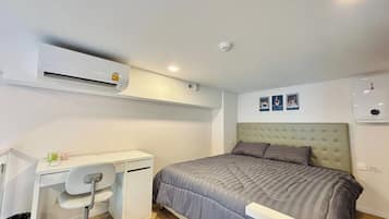 A bedroom with a bed, a desk, and an air conditioning unit.