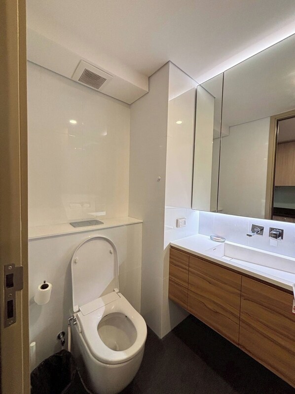 Un baño moderno con inodoro, lavamanos y espejo.