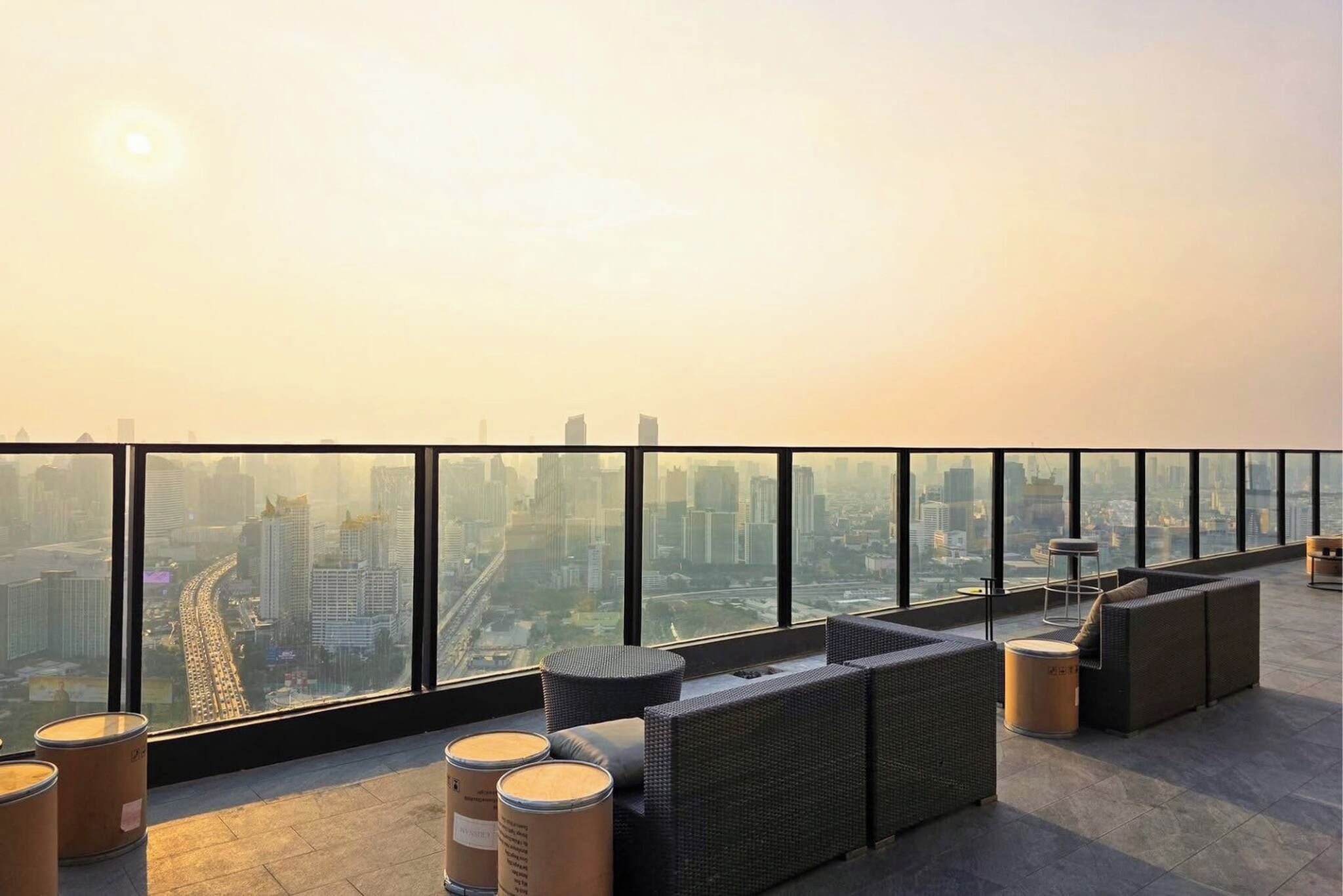 Terraço no telhado com vista para a cidade, mobiliado com sofás de vime e mesas redondas.