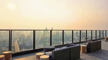 Terraço no telhado com vista para a cidade, mobiliado com sofás de vime e mesas redondas.