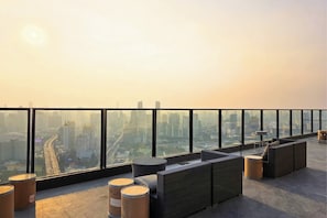 Terraço no telhado com vista para a cidade, mobiliado com sofás de vime e mesas redondas.
