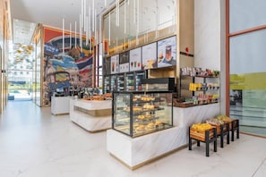 Uma praça de alimentação com diversos quiosques, um mural na parede e uma área de estar com mesas e cadeiras.