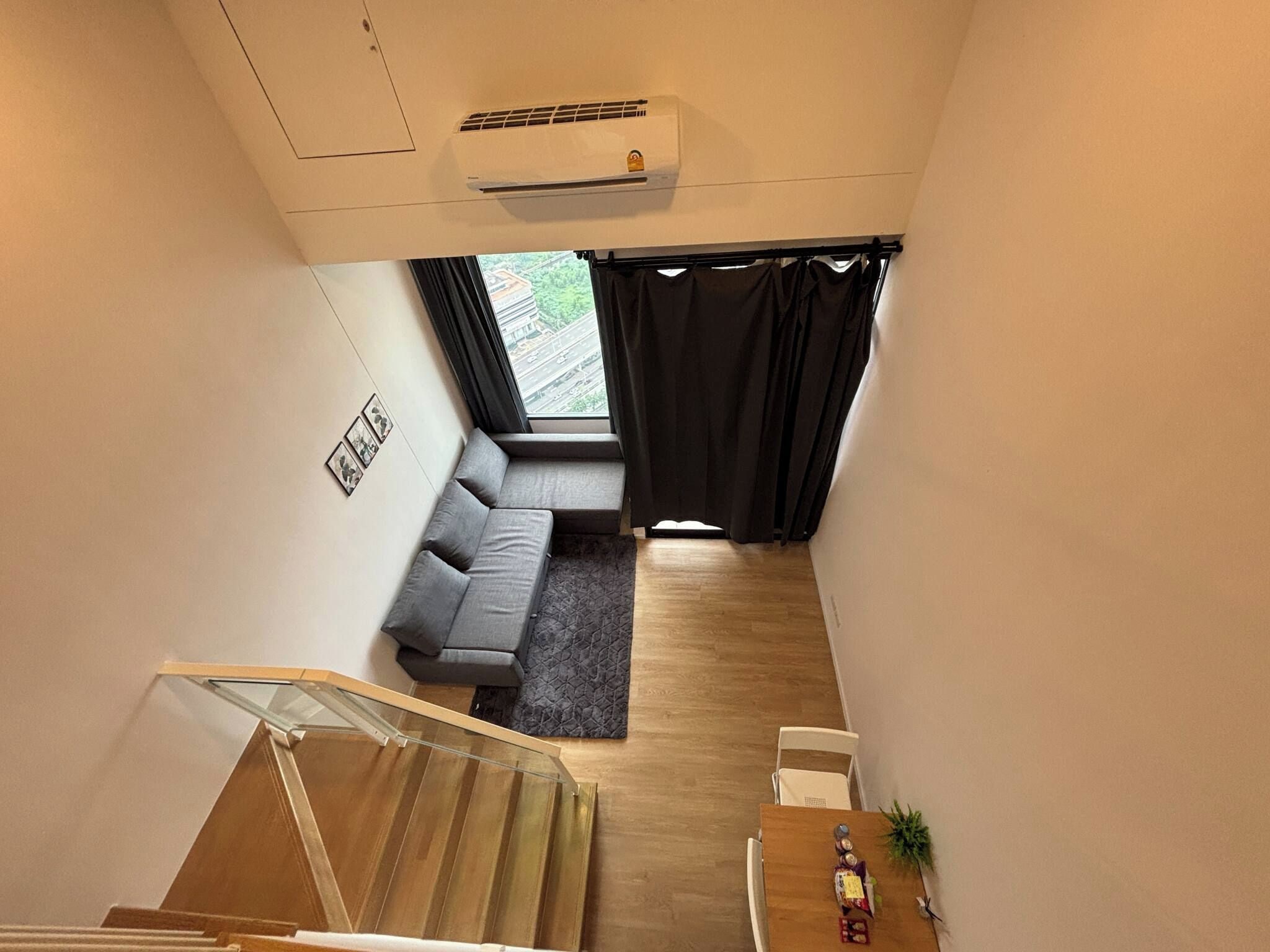 A modern living room with a grey sofa, a small rug, and a staircase leading to an upper floor.