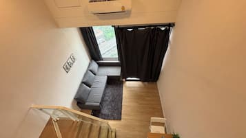 A modern living room with a grey sofa, a small rug, and a staircase leading to an upper floor.