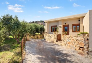 A stone house with a gravel driveway, a wooden gate, and potted plants. - Anezina – Cretan Hospitality in Agriana, near Analipsi Beach (Agriana)