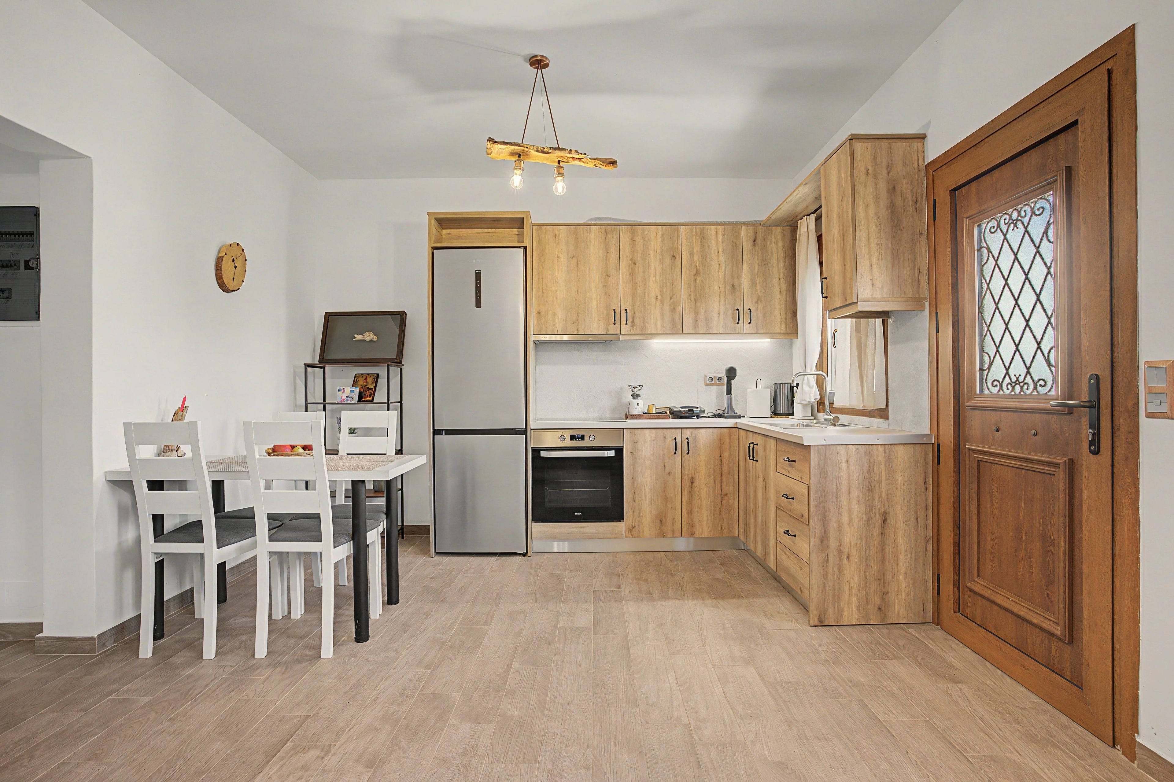 Une cuisine moderne avec des meubles en bois, un four encastré et un coin repas avec des chaises blanches.