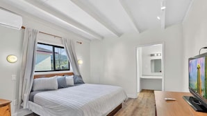 Un dormitorio con cama, televisor, escritorio y ventana con cortinas.