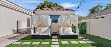 Ein Schlafzimmer im Freien mit zwei Betten, einem geflasterten Dach, weißen Vorhängen und einem Rasen.