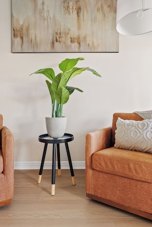 A living room with a potted plant on a small table, a sofa, and a painting on the wall. - New Luxe 5BR Resort | Pool, Pickleball | Theater (Mesa)
