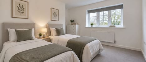 Une chambre avec deux lits, une table de chevet, une commode, un radiateur et une fenêtre donnant sur un beau paysage.
