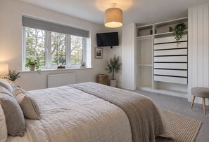 A bedroom with a bed, a window with a view, a television, and a built-in wardrobe. - Stylish 4-Bed Home in Wokingham | Parking & Garden Office (Winnersh)