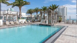 A rooftop pool area with lounge chairs, palm trees, and a view of the city skyline. - Spacious 3BDR condo with Panoramic Luxury Getaway - NO RESORT & PARKING FEE (Hollywood)