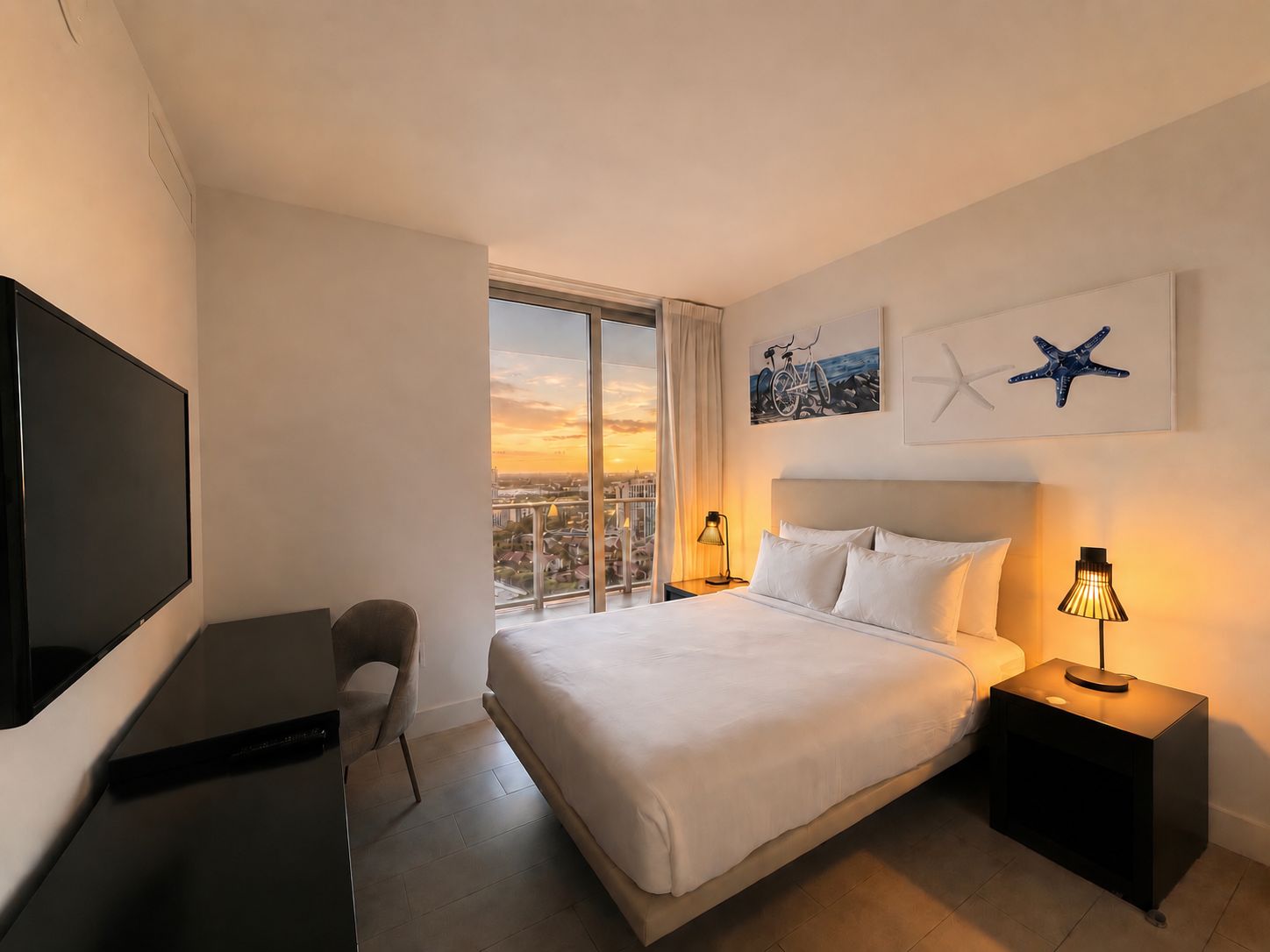 A hotel room with a bed, a TV, a chair, a nightstand with a lamp, and a large window with a city view.