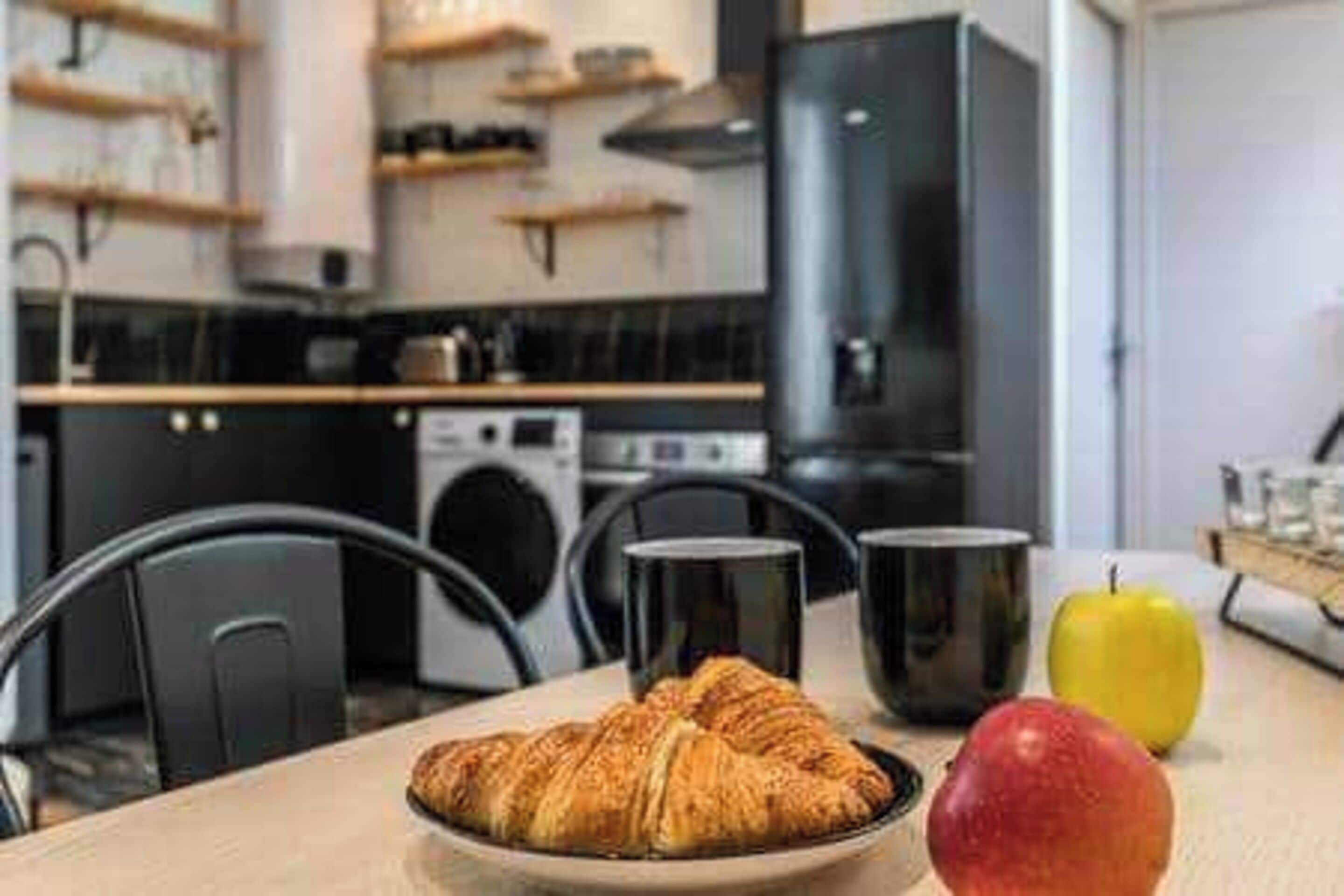 A kitchen with a table set for breakfast, including croissants, a mug, and an apple.