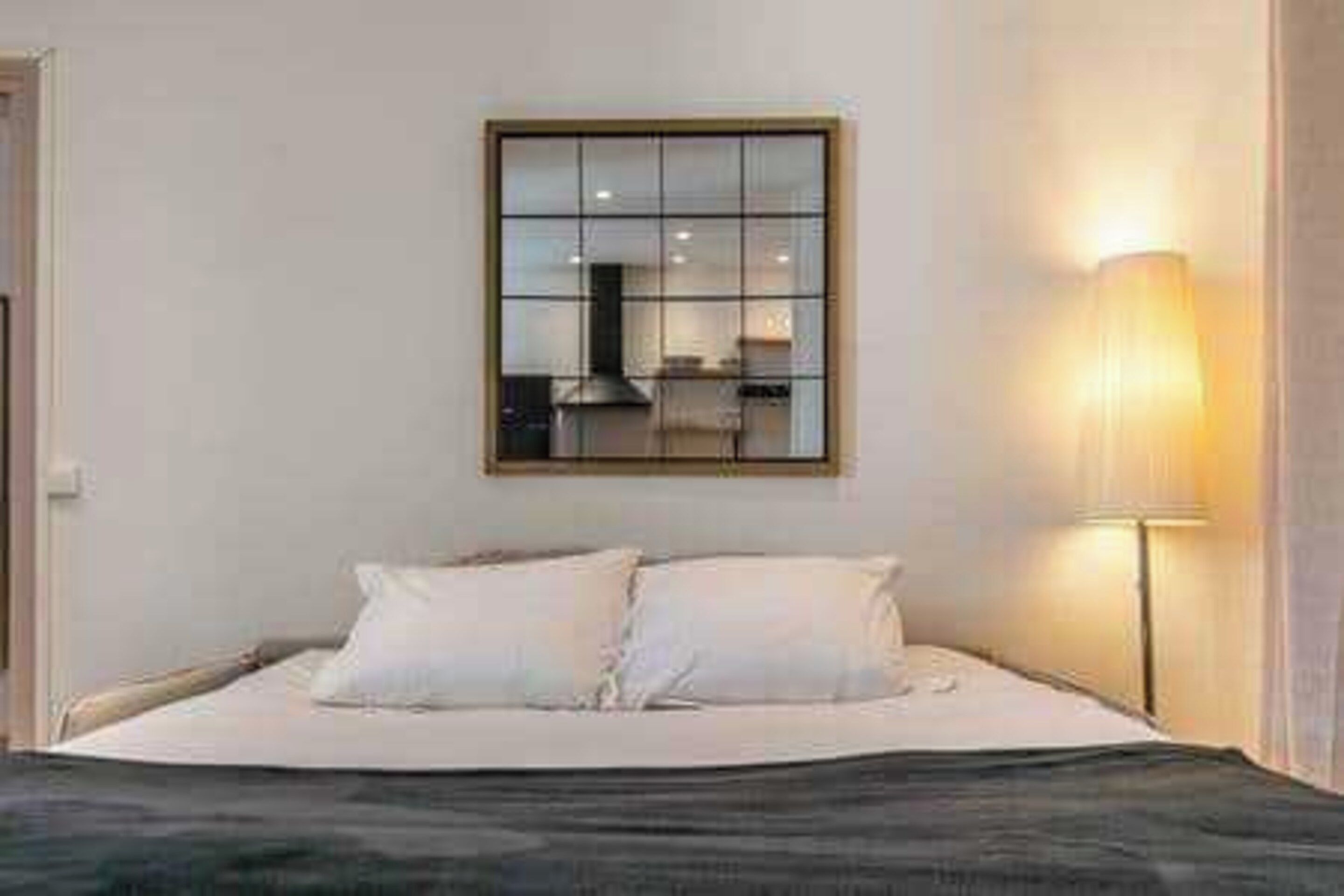 A bed with white bedding, a bedside lamp, and a window with blinds.