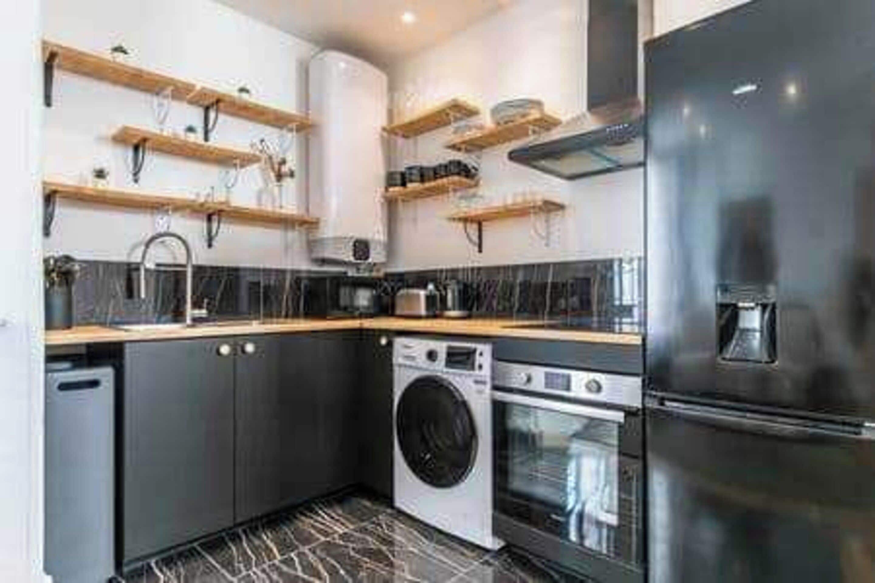 A modern kitchen with built-in appliances, wooden shelves, and a black and white tiled floor.