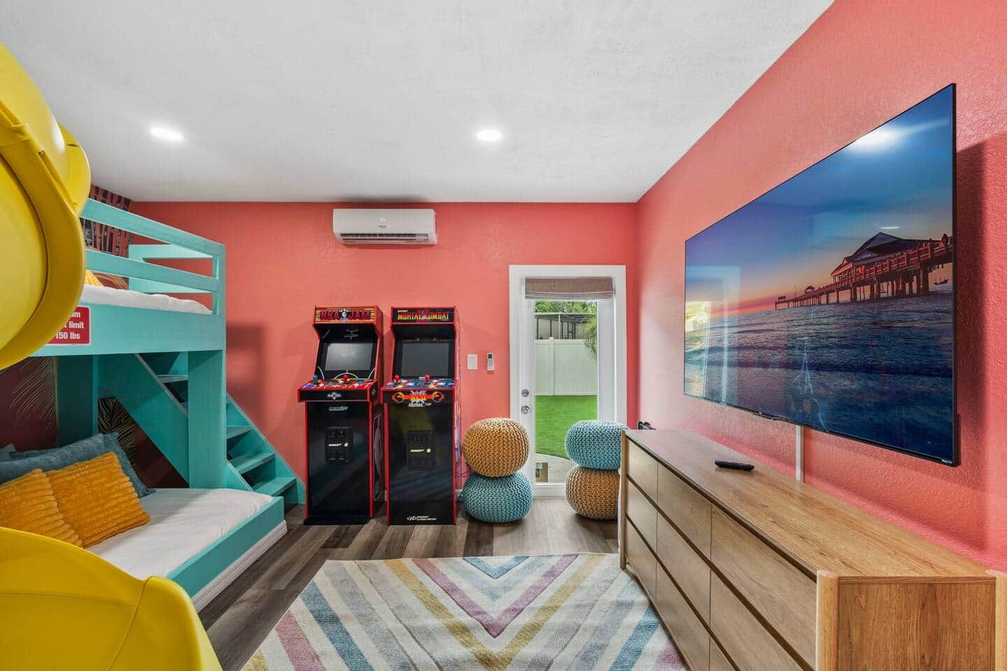 Een kamer met stapelbedden, speelautomaten, een grote televisie en een kleurrijk vloerkleed.