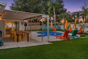 Un jardin avec une piscine, un espace salon extérieur et une terrasse couverte.
