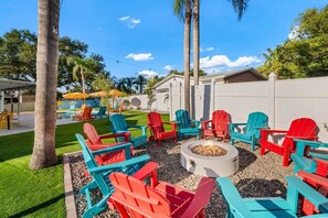 An outdoor seating area with Adirondack chairs arranged around a fire pit. - Playcation Oasis (Pinellas County)